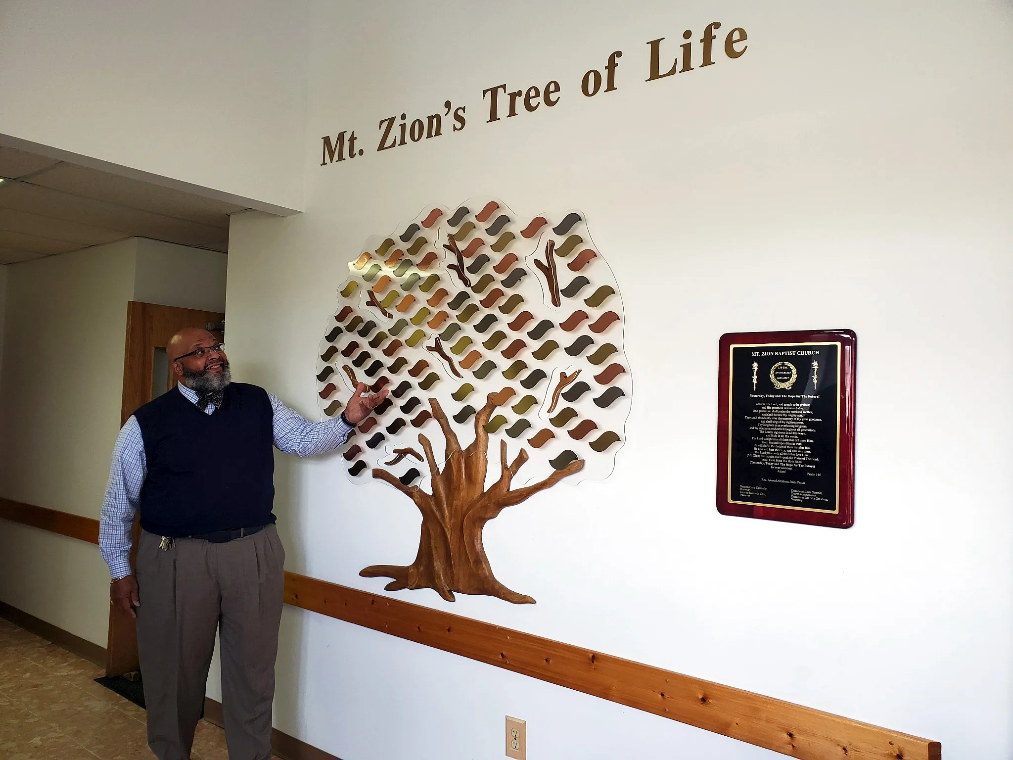 Mt. Zion's Tree of Life on the church wall, with a church leader beside it.