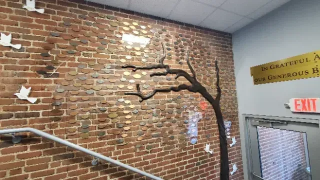 A B&D custom donor recognition tree with engraved metal leaves fanning across a branded acrylic panel, designed and installed for a Harrisburg Catholic organization.