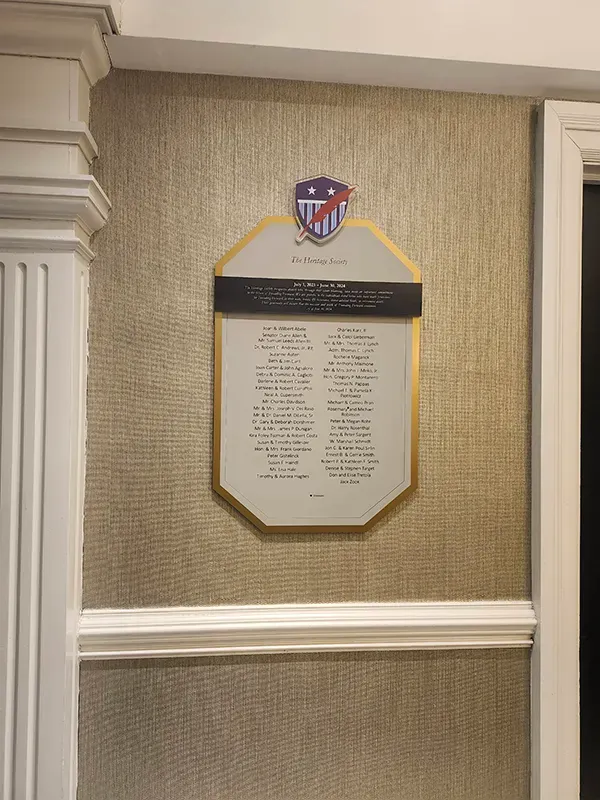 A B&D “Heritage Society” donor plaque with an engraved donor list beneath a shield crest, mounted on a grasscloth wall.