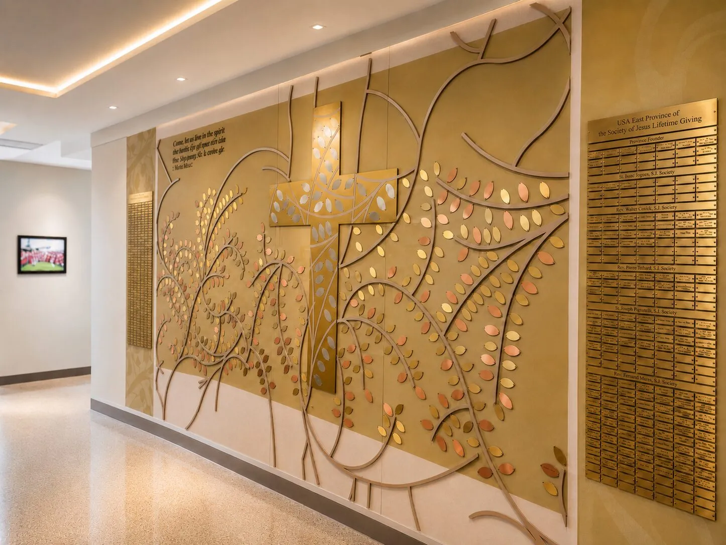 A B&D sculptural donor recognition wall featuring a gold cross and tree-of-life design holding engraved metal leaves, beside a lifetime-giving name plaque.